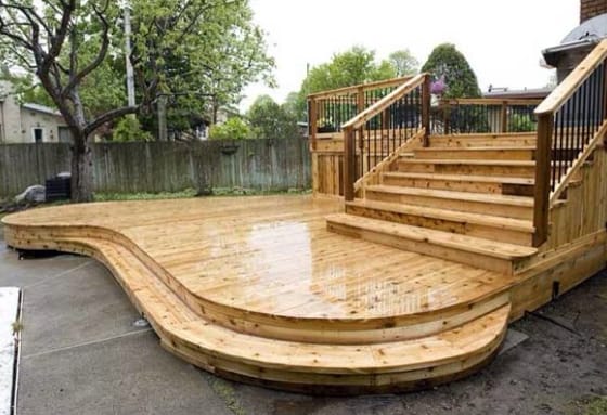 Large, curvy pine deck with stairs leading to another deck at back of a house.